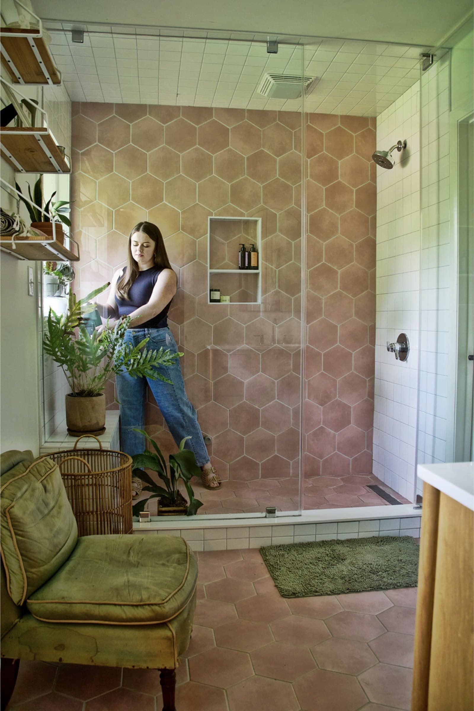 A woman watering plants in a pink tiled shower